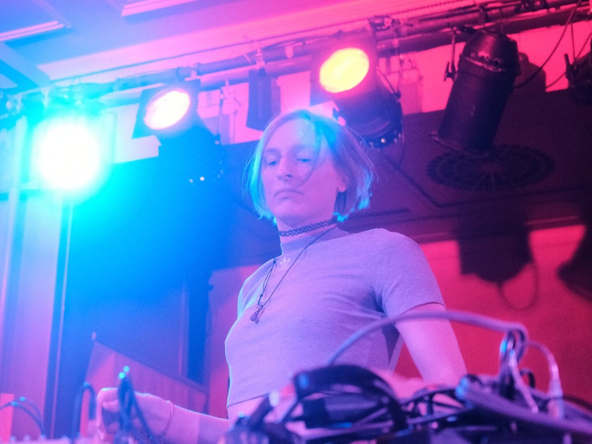 Jeanne Artemis performing live with hardware synthesizers, lit in pink and blue stage light